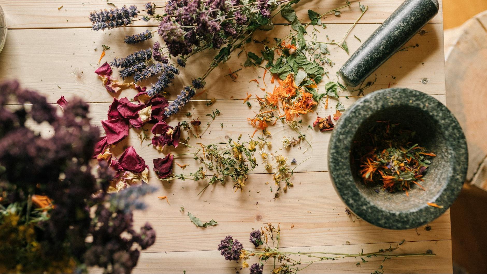 Decorative image of dried herbs and flowers in a wooden table with a pestle and mortar 